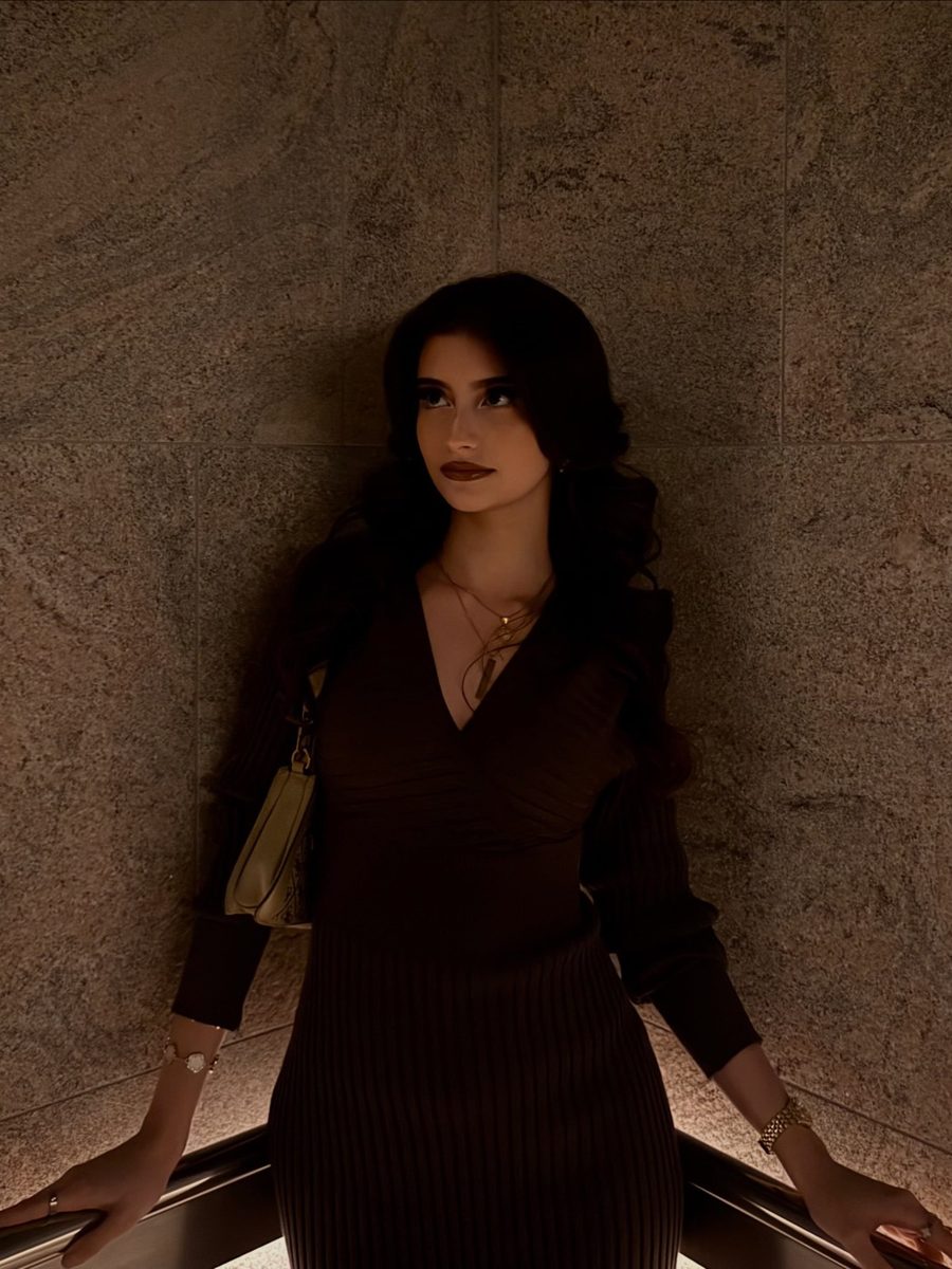 Aisha leaning against a lit stone wall in an espresso ribbed knit dress.